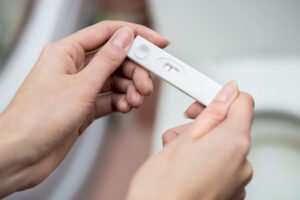 Duas mãos femininas segurando um teste de gravidez de farmácia