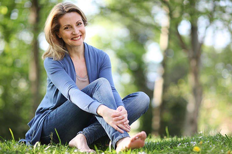 Mulher de meia idade sorrindo, sentada no gramado de um parque