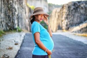 Gravidez na adolescência, jovem grávida de chapéu atravessando uma estrada