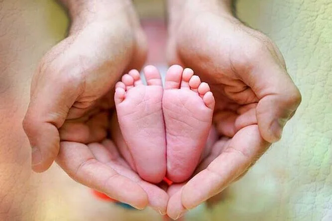 Dois pézinhos de bebê entre as mãos da mãe