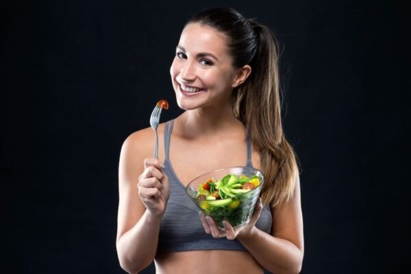 Mulher jovem e bonita comendo uma salada, fotografada sobre fundo preto